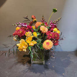 Mixed bouquet of yellow, pink, and orange flowers in a glass vase