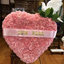 Pink carnation heart arrangement with a white dove topper and ribbon