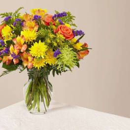 Mixed bouquet of yellow, orange, and purple flowers in a glass vase