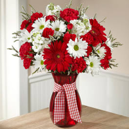 Red and white mixed bouquet in a red glass vase with a gingham ribbon