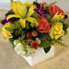 Mixed bouquet with yellow lilies, roses, and purple orchids in a white box