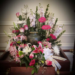 Pink and white funeral flowers arranged around an urn on a casket