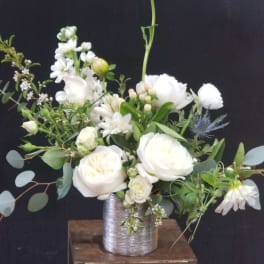 White floral arrangement in a silver vase on a wooden stand