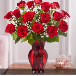 Red roses arranged in a red glass vase with white baby's breath