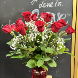 Red roses arranged in a red glass vase with white baby's breath