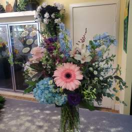 Mixed bouquet in a glass vase with pink gerbera, blue hydrangea, and white lilies