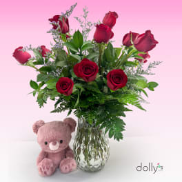 Red roses in a glass vase with a pink teddy bear beside it