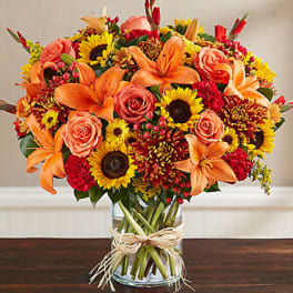 Orange lilies, roses, and sunflowers in a glass vase