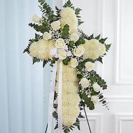 White floral standing cross with roses and greenery on an easel