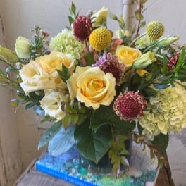 Yellow roses and pale hydrangeas in a glass vase with round accent blooms