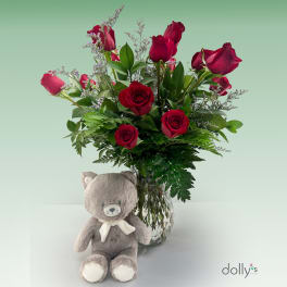 Red roses in a glass vase with a gray teddy bear in front
