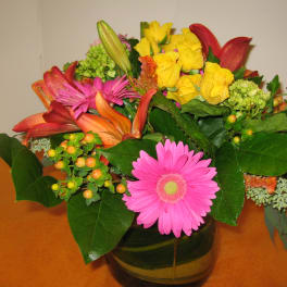 Mixed bouquet of yellow roses, pink gerbera daisies, and lilies in a glass vase