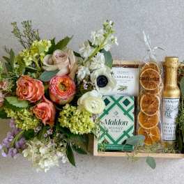 Floral bouquet beside a gift tray with caramels, sea salt, crisps, and olive oil
