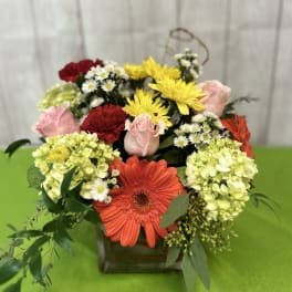 Mixed bouquet in a square glass vase with gerbera daisies, roses, and hydrangeas