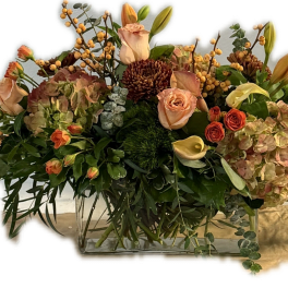 Mixed floral arrangement in a clear rectangular vase with roses and lilies