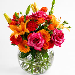 Bright mixed bouquet of roses, lilies, and carnations in a clear glass vase