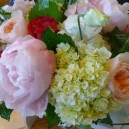 Round arrangement of pale pink peonies, roses, and cream hydrangeas with accents of red roses