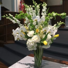 White flowers and yellow tulips arranged in a clear glass vase