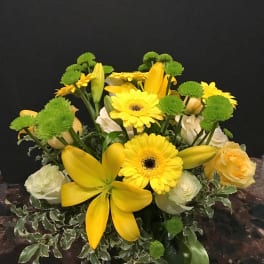 Yellow lilies and gerbera daisies with green button mums in a vase