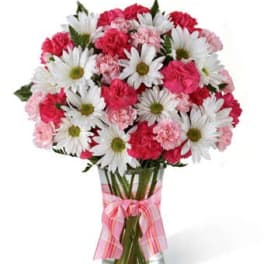 Bouquet of pink carnations and white daisies in a glass vase with a pink ribbon