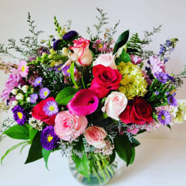 Mixed bouquet of roses, calla lilies, and purple daisies in a glass vase