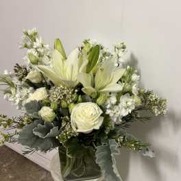 White lilies and roses arranged in a glass vase with silver foliage