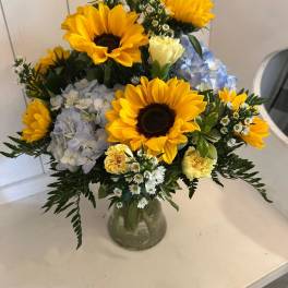 Bouquet of sunflowers, hydrangeas, and small white flowers in a glass vase