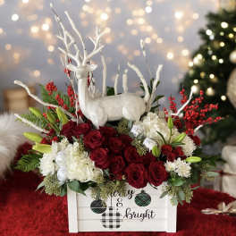 Holiday floral arrangement with red roses and a white deer figurine in a wooden box