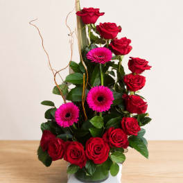 Red roses and pink gerbera daisies arranged in a glass vase