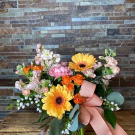 Bouquet of orange roses and yellow gerbera daisies in a glass vase with a pink ribbon