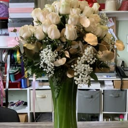 Cream roses in a tall green glass vase with gold-toned foliage