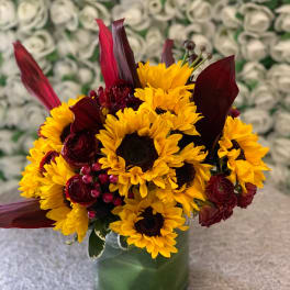 Sunflowers and burgundy flowers arranged in a green glass vase