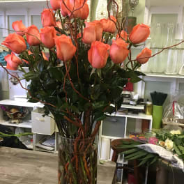 Tall vase arrangement of coral roses with curly branches