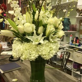 Tall white floral arrangement in a green glass vase