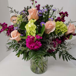 Mixed bouquet of peach roses, purple asters, and green hydrangea in a glass vase