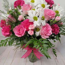 Pink roses, white daisies, and carnations in a glass vase with a polka-dot ribbon