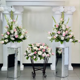 Three pink and white floral arrangements displayed on pedestals