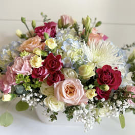 Mixed bouquet of pink, red, and white flowers in a low white container