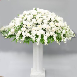 Large white floral arrangement in a tall white pedestal vase
