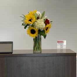 Sunflower bouquet in a tall glass vase with white and red flowers