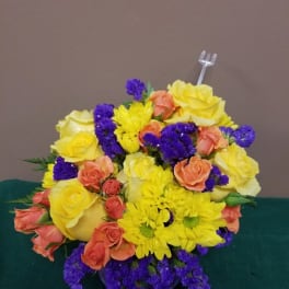 Bouquet of yellow and peach roses with purple filler flowers in a low vase