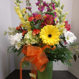 Mixed bouquet in a green vase with a large orange ribbon