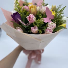 Handheld bouquet of pink, yellow, and purple tulips wrapped in pale paper