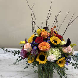 Mixed bouquet of roses, sunflowers, and calla lilies in a glass vase