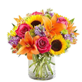 Mixed bouquet of sunflowers, orange lilies, and pink roses in a glass vase
