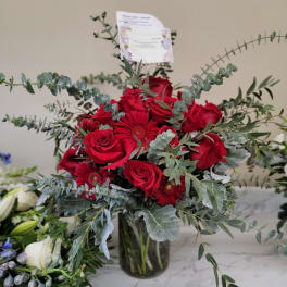 Red roses and gerbera daisies in a glass vase with airy eucalyptus