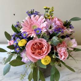 Mixed pink and purple flower arrangement in a square vase