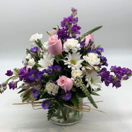 Mixed bouquet of pink roses, white daisies, and purple flowers in a glass vase