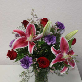 Bouquet of pink lilies, red roses, and purple flowers in a glass vase