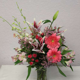 Mixed bouquet in a glass vase with pink gerbera daisies, lilies, and roses